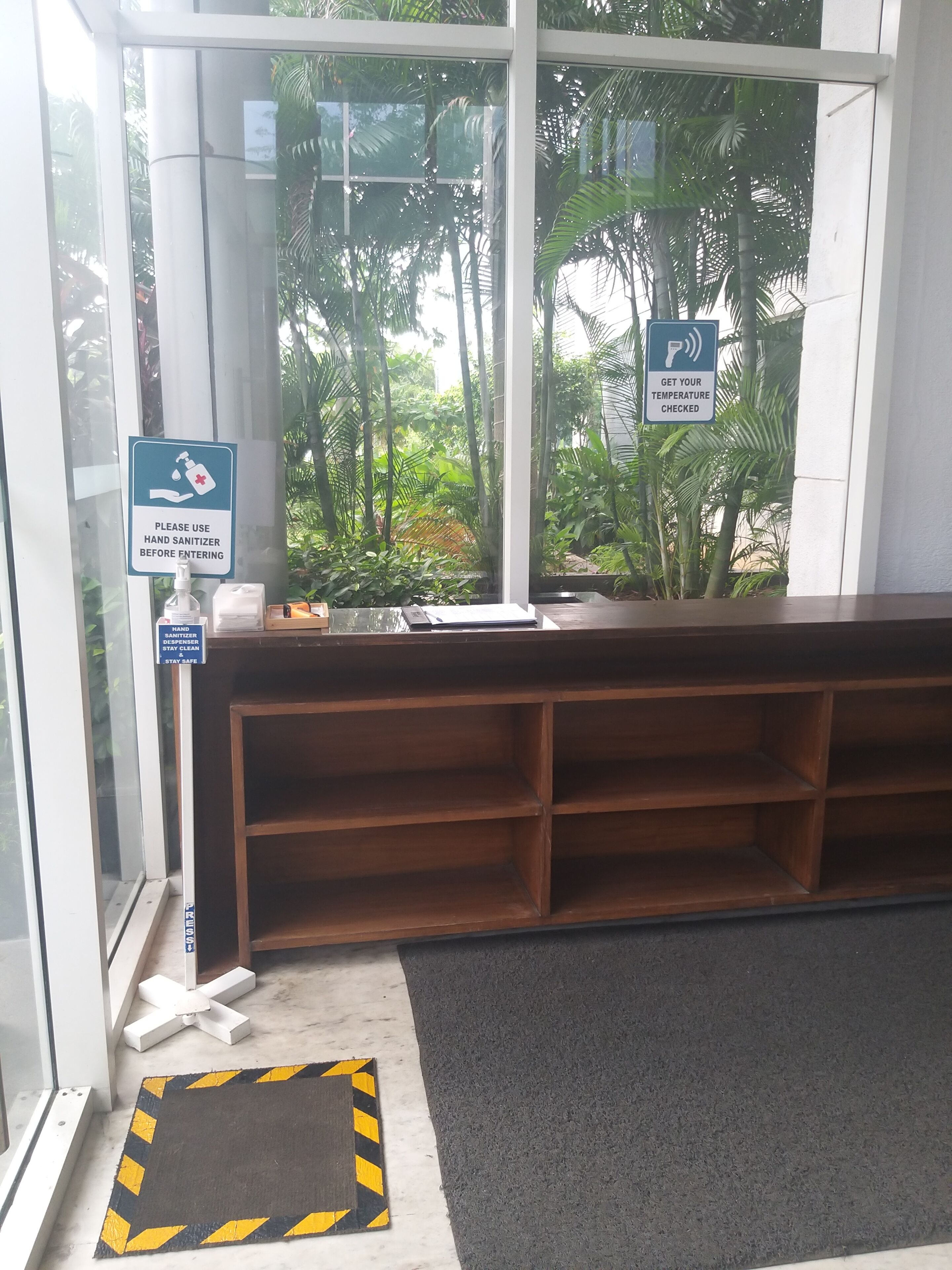 A reception area with a hand sanitizer dispenser, a temperature check station, and a view of lush greenery outside.