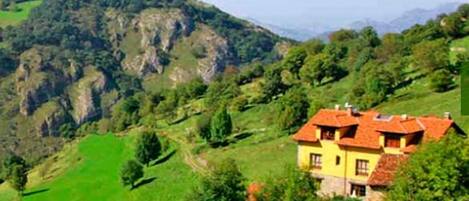 A yellow house with a red roof nestled in a green valley surrounded by hills.