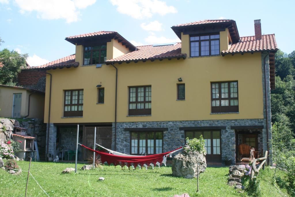 A two-story house with a yellow facade, stone base, and red-tiled roof.