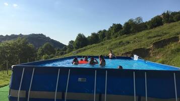 Piscina rectangular con una escalera en un lado, rodeada de césped, árboles y colinas al fondo.