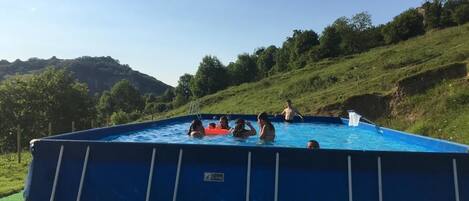 Piscina rectangular con una escalera en un lado, rodeada de césped, árboles y colinas al fondo.
