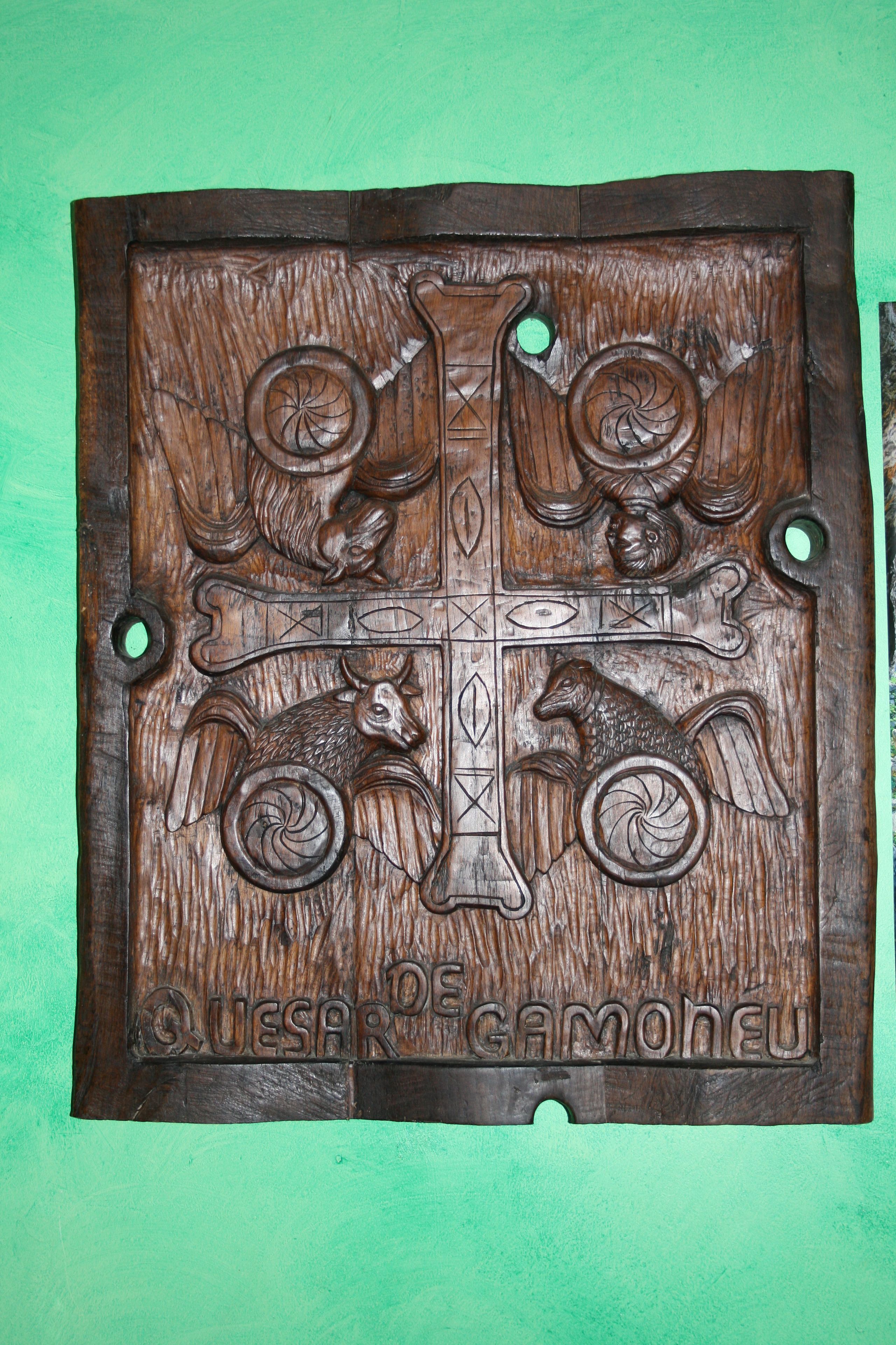 Una placa de madera con diseños tallados y la inscripción 'Quesar de Gamoneu'.