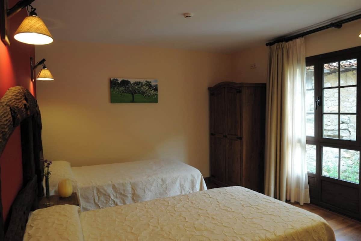 Een kamer met twee bedden, een houten garderobe, een schilderij aan de muur en een raam met gordijnen.