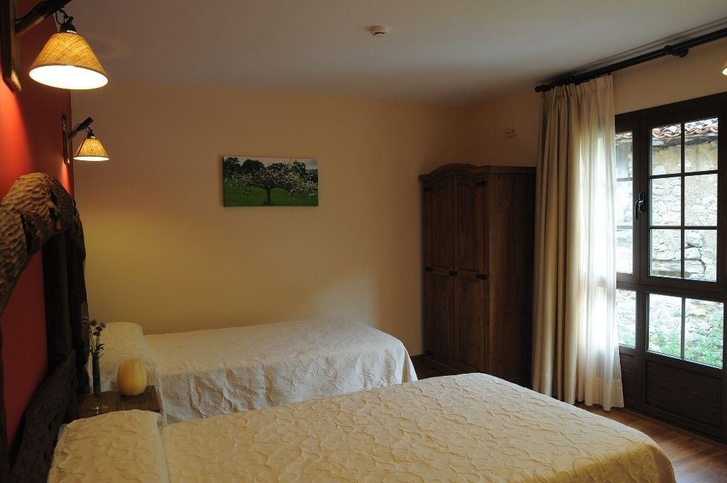 Un dormitorio con dos camas, un armario de madera, un cuadro en la pared y una ventana con cortinas.