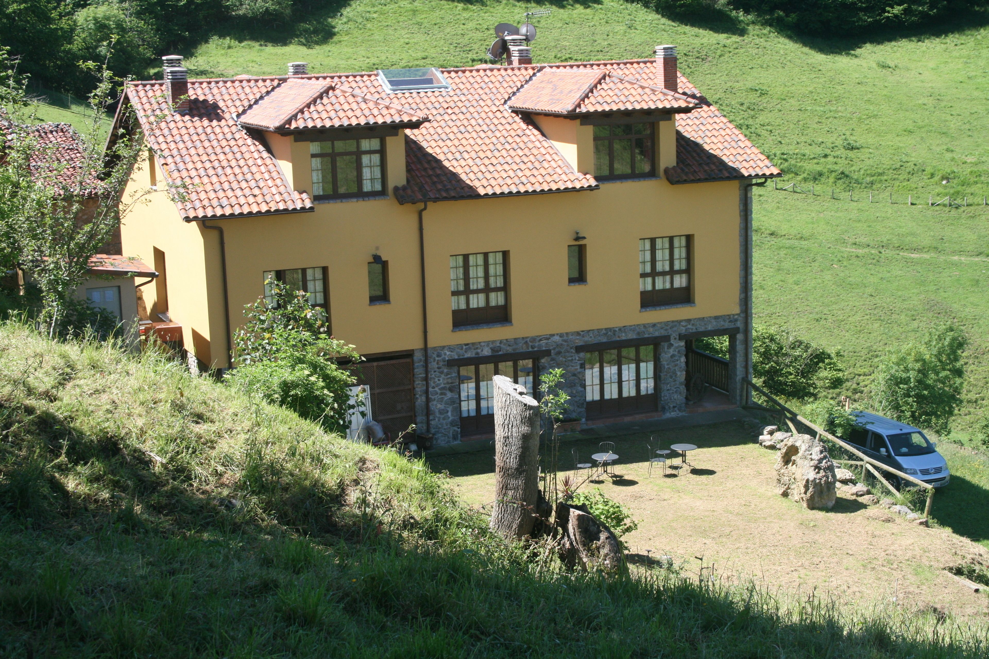 Ein zweistöckiges Haus mit Ziegeldach, Steinunterbau und einer kleinen Terrasse mit Gartenmöbeln.