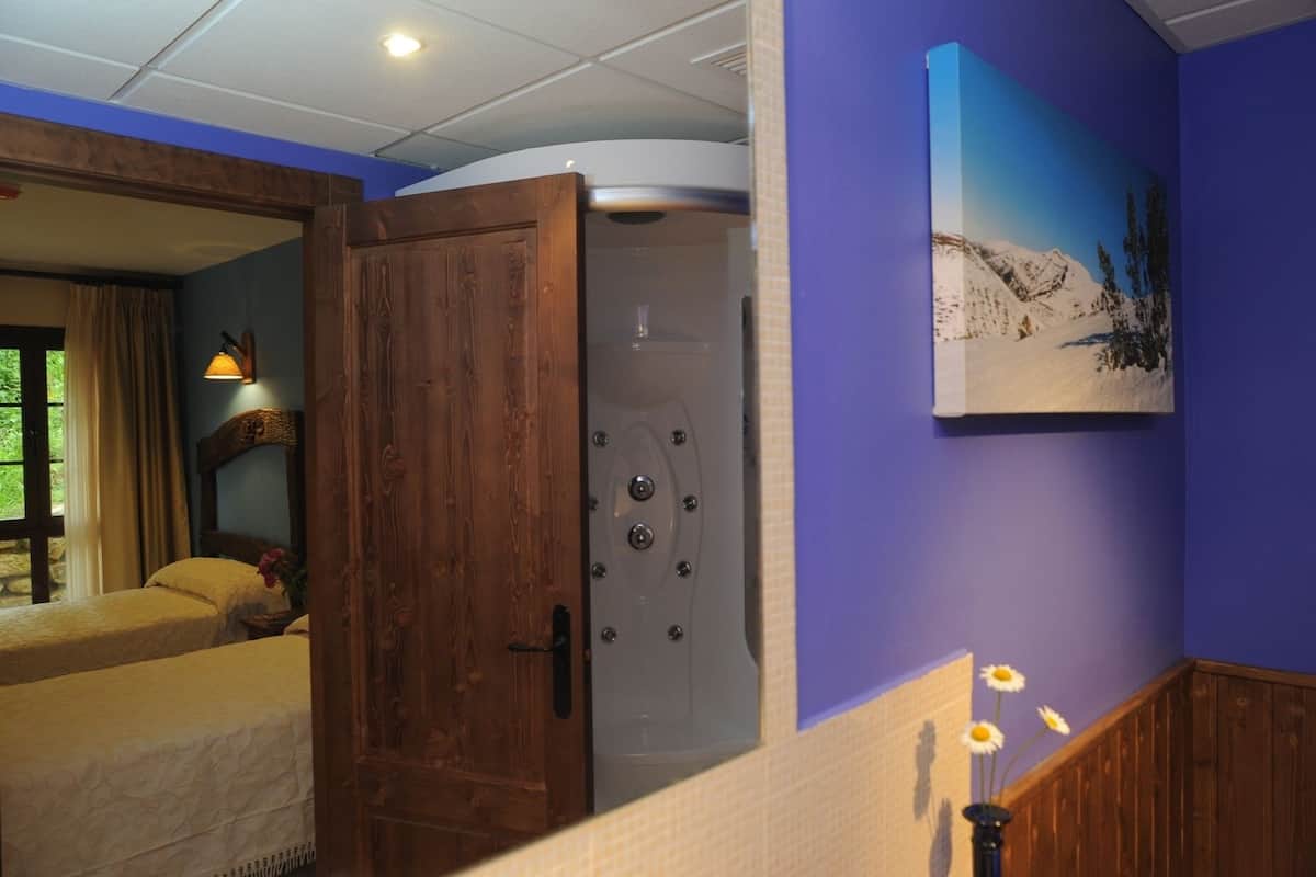 Een kamer met een houten deur, een bed, een douche en een schilderij aan de muur.