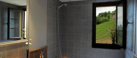 Un baño moderno con bañera, lavamanos y ducha. Hay una ventana con vistas a un paisaje verde.