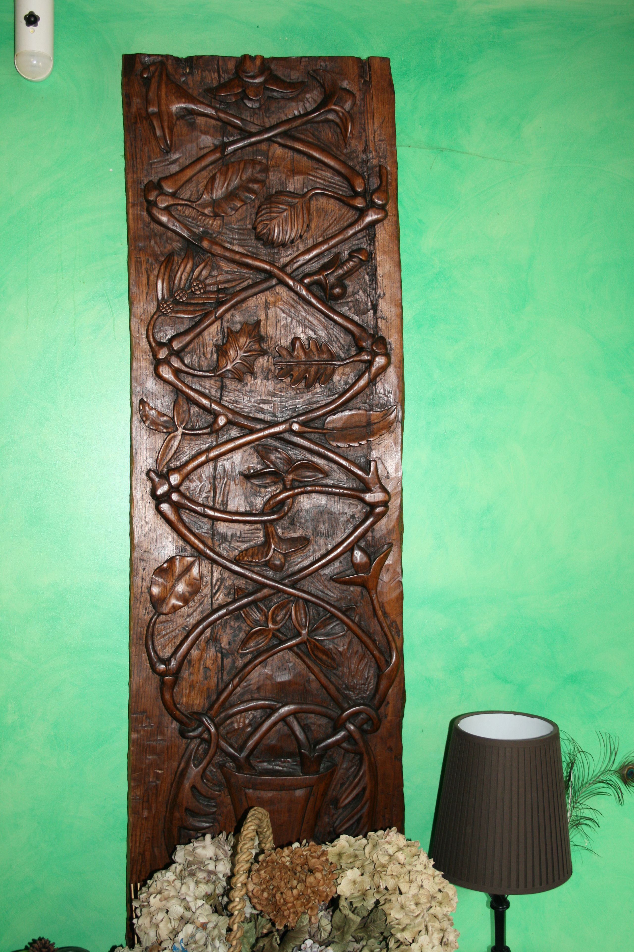 Een houten sculptuur met ingewikkelde decoraties, een lamp en een bloevas tegen een groene muur.