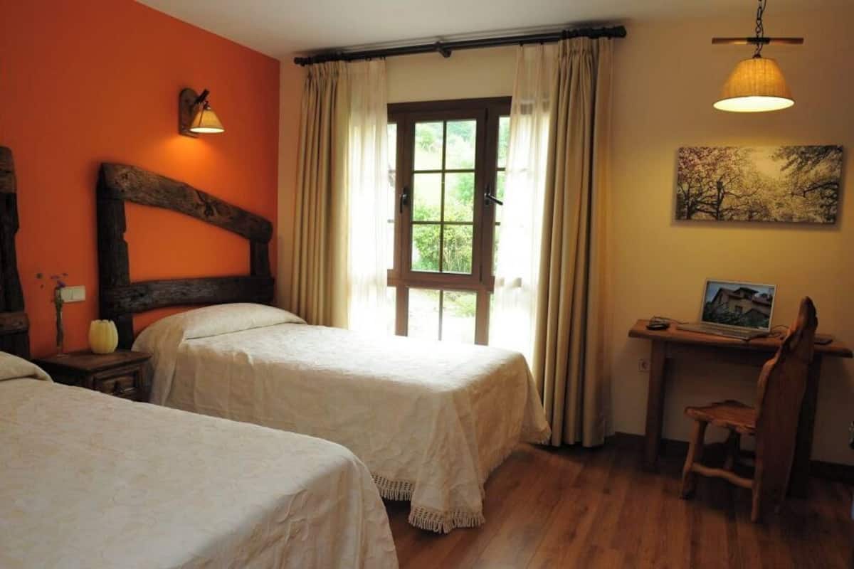 Een kamer met twee bedden, een bureau met een laptop, een lamp en een schilderij aan de muur.