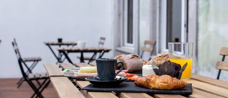 A breakfast setup with a croissant, a muffin, a glass of orange juice, and a cup on a wooden table.