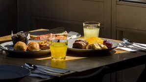 Taula de matí amb pastissos, un got de suc d'aranja, i vista a una cadira a través d'una finestra.