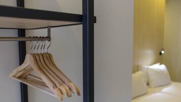 Quarto de hotel com cama, almofadas brancas e um porta-roupas de madeira com roupas.