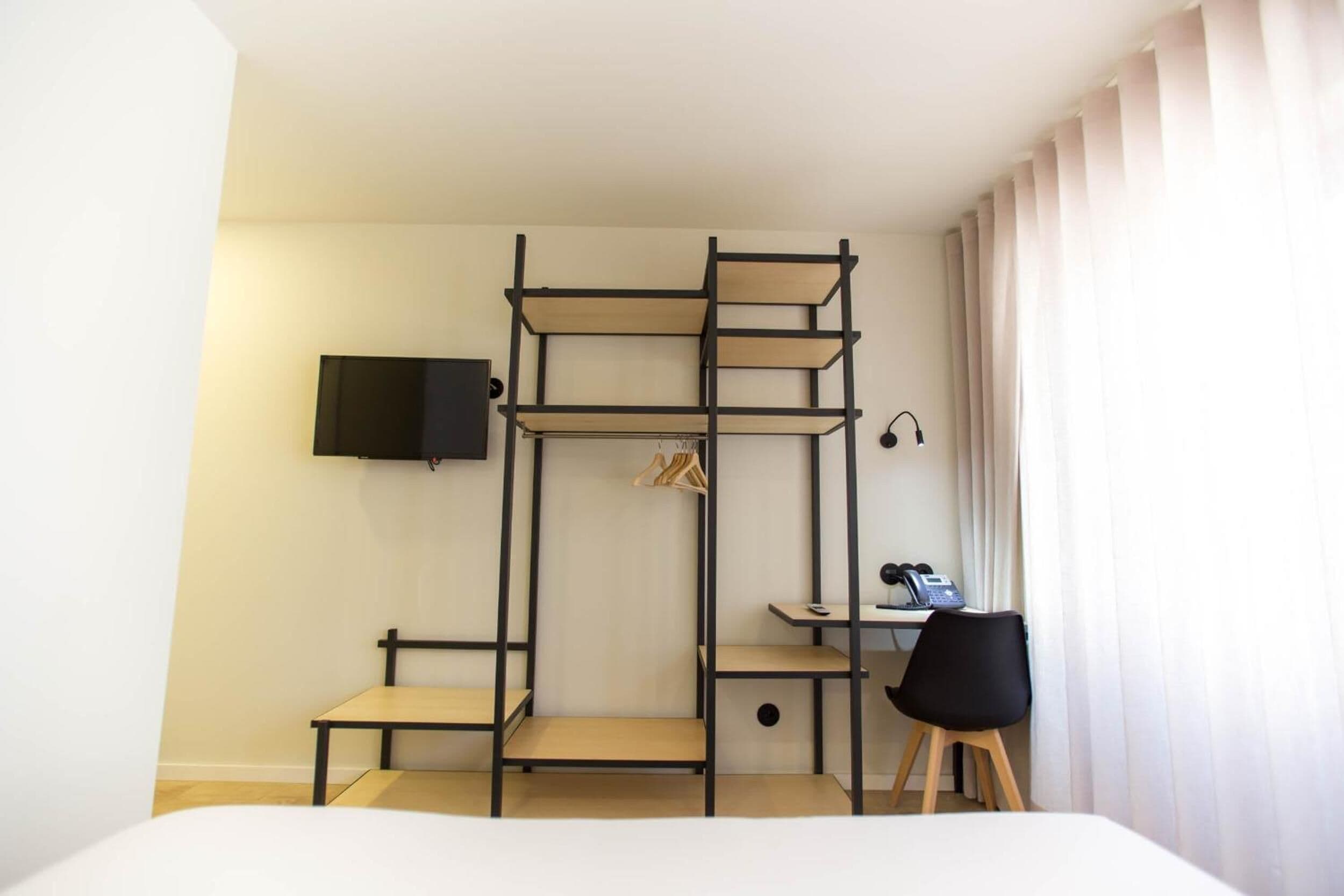 A hotel room with a bunk bed, a desk with a chair, a TV mounted on the wall, and a window with curtains.