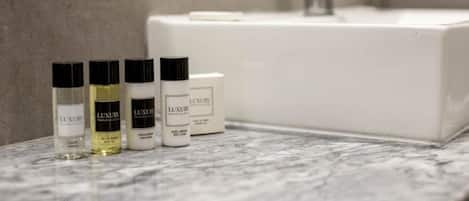 A bathroom with a white sink, a mirror, and three bottles of 'LUXURY' body lotion.