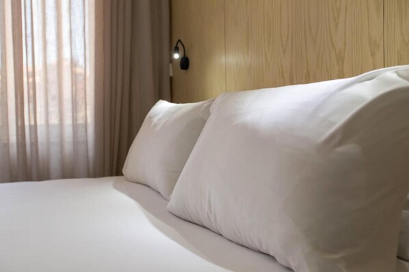 Un lit bien fait, avec du linge de lit blanc et des oreillers, une tête de lit en bois et un luminaire fixé au mur.