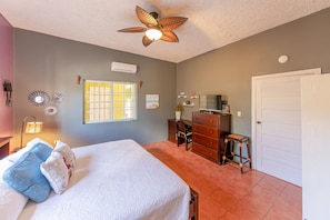 A bedroom with a bed, a desk, a chair, a dresser, a ceiling fan, and a window.