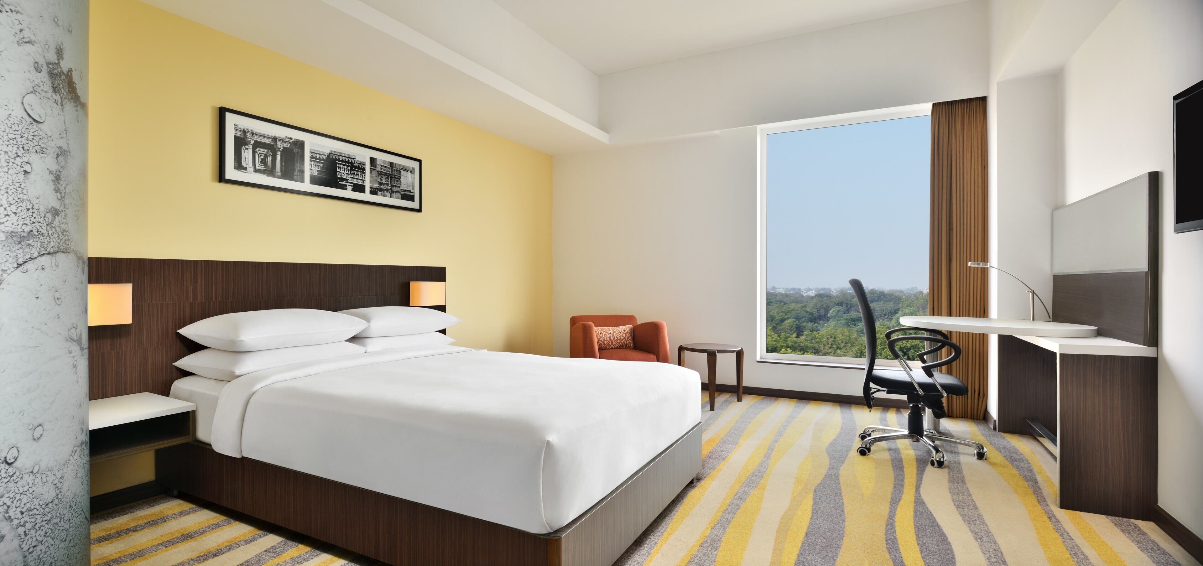 Une chambre d’hôtel équipée d’un lit, d’un bureau, d’une chaise, d’une télévision et d’une fenêtre donnant sur un paysage agréable.
