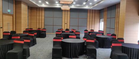 Een congreszaal met ronde tafels en stoelen, een vloerbedekking, houten paneelwanden en inbouw plafondverlichting.