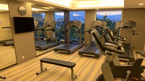 Un gimnasio con cintas de correr, una banca y un televisor en la pared.