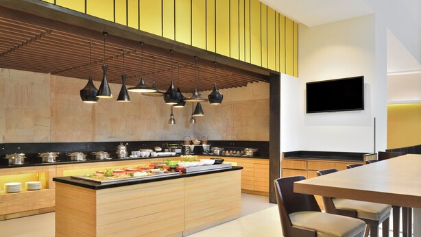 Una cocina moderna con una isla central, iluminación colgante y un televisor de pantalla plana montado en la pared.