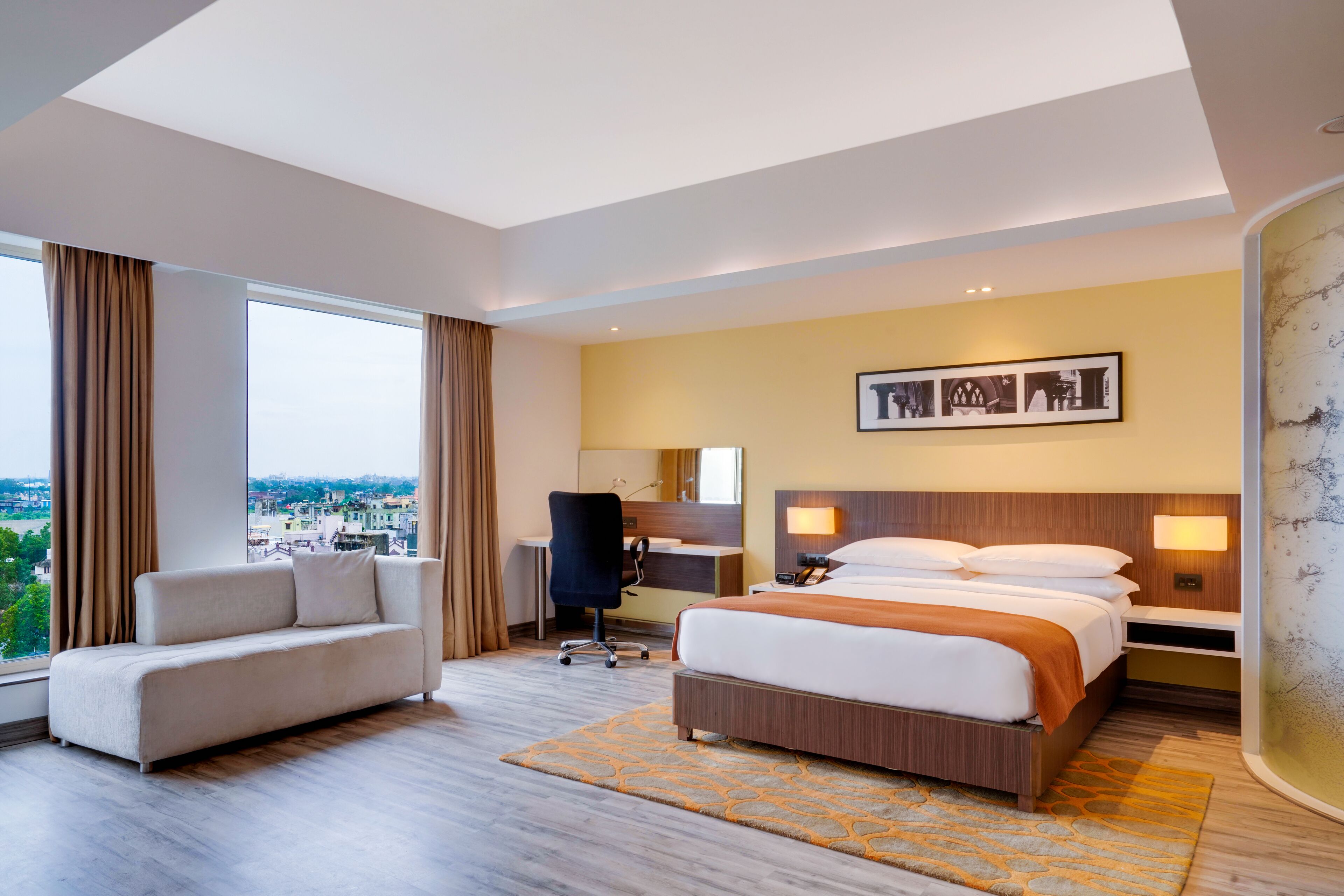 A modern hotel room with a large bed, a sofa, a desk, and a view of the city.