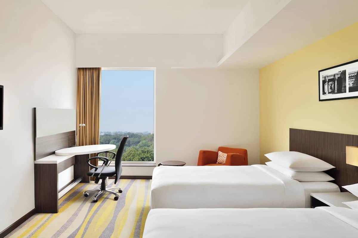 Ein Hotelzimmer mit einem großen Bett, einem Schreibtisch mit Stuhl, einem kleinen Tisch und einem Fenster mit Blick ins Grüne.