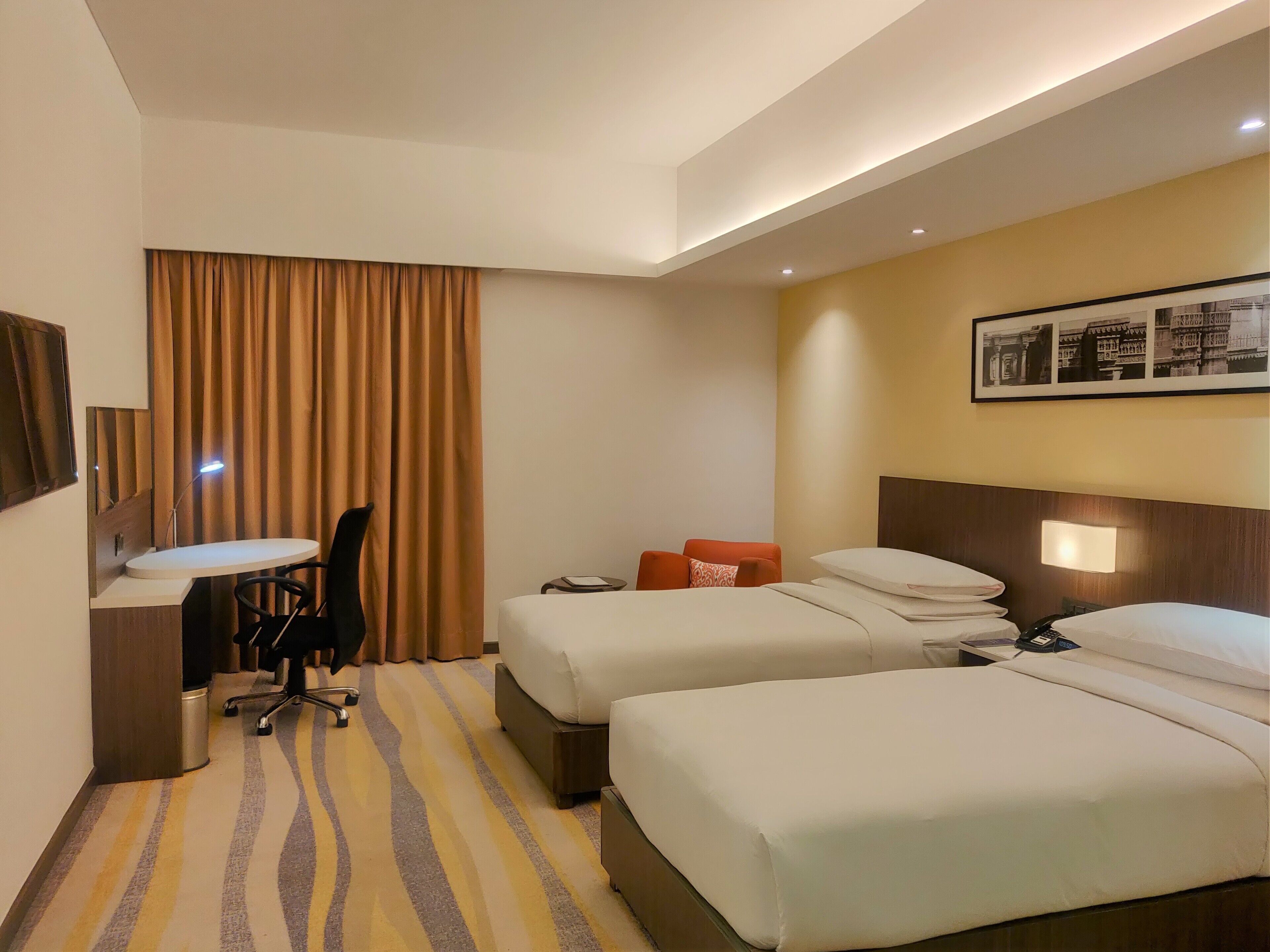 Habitació d'hotel amb dos llits, una taula, una cadira i un gran finestral amb cortines.