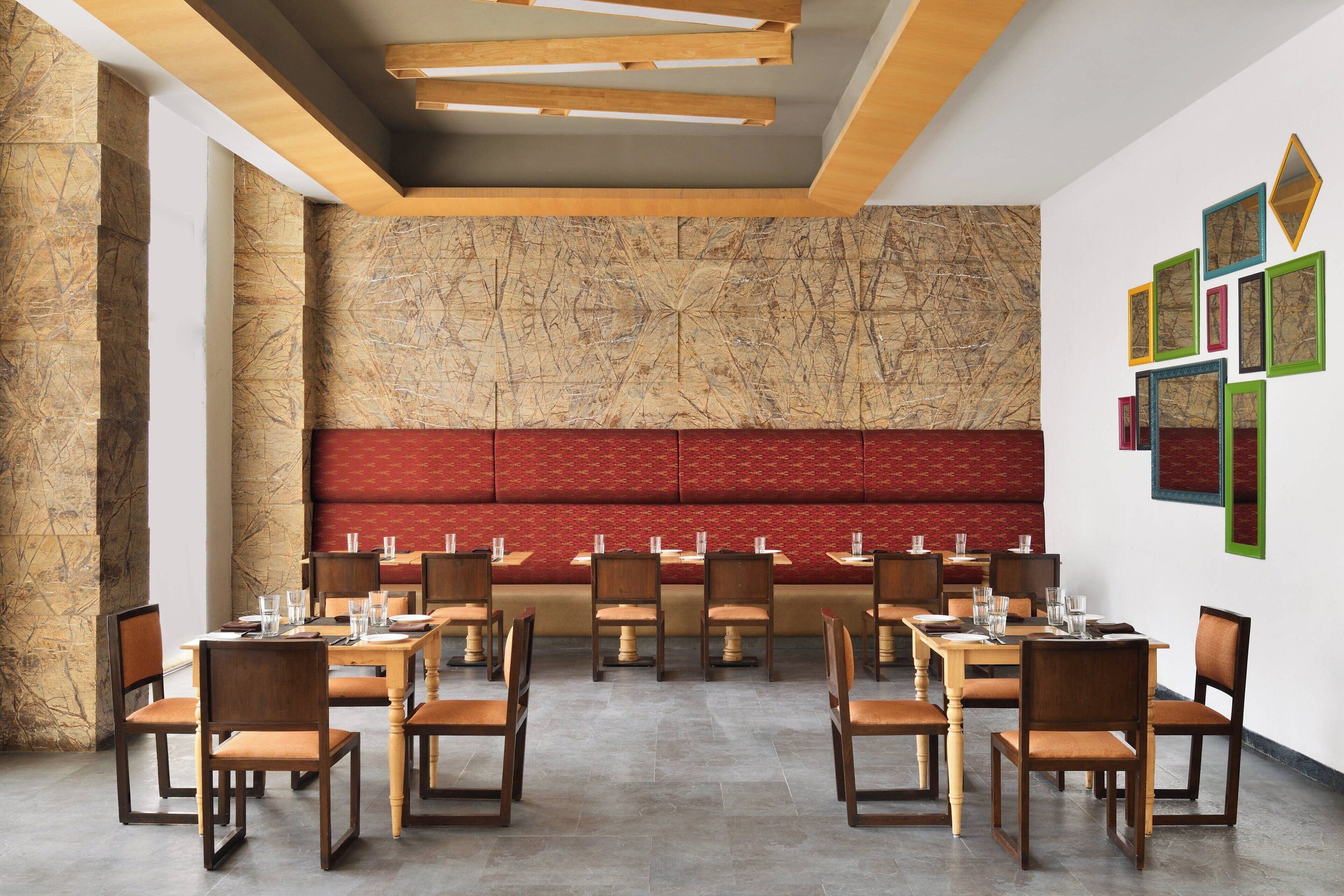 Un espace repas avec des tables et des chaises en bois, un banc rouge rembourré et un mur décoré d’un motif marbré.