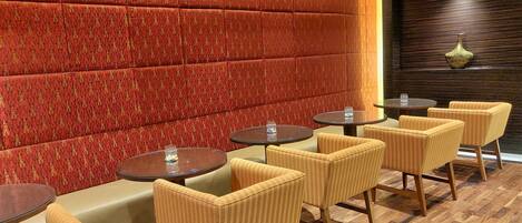 Un área de descanso moderna con asientos acolchados y mesas redondas, con un revestimiento de pared estampado y suelo de madera.
