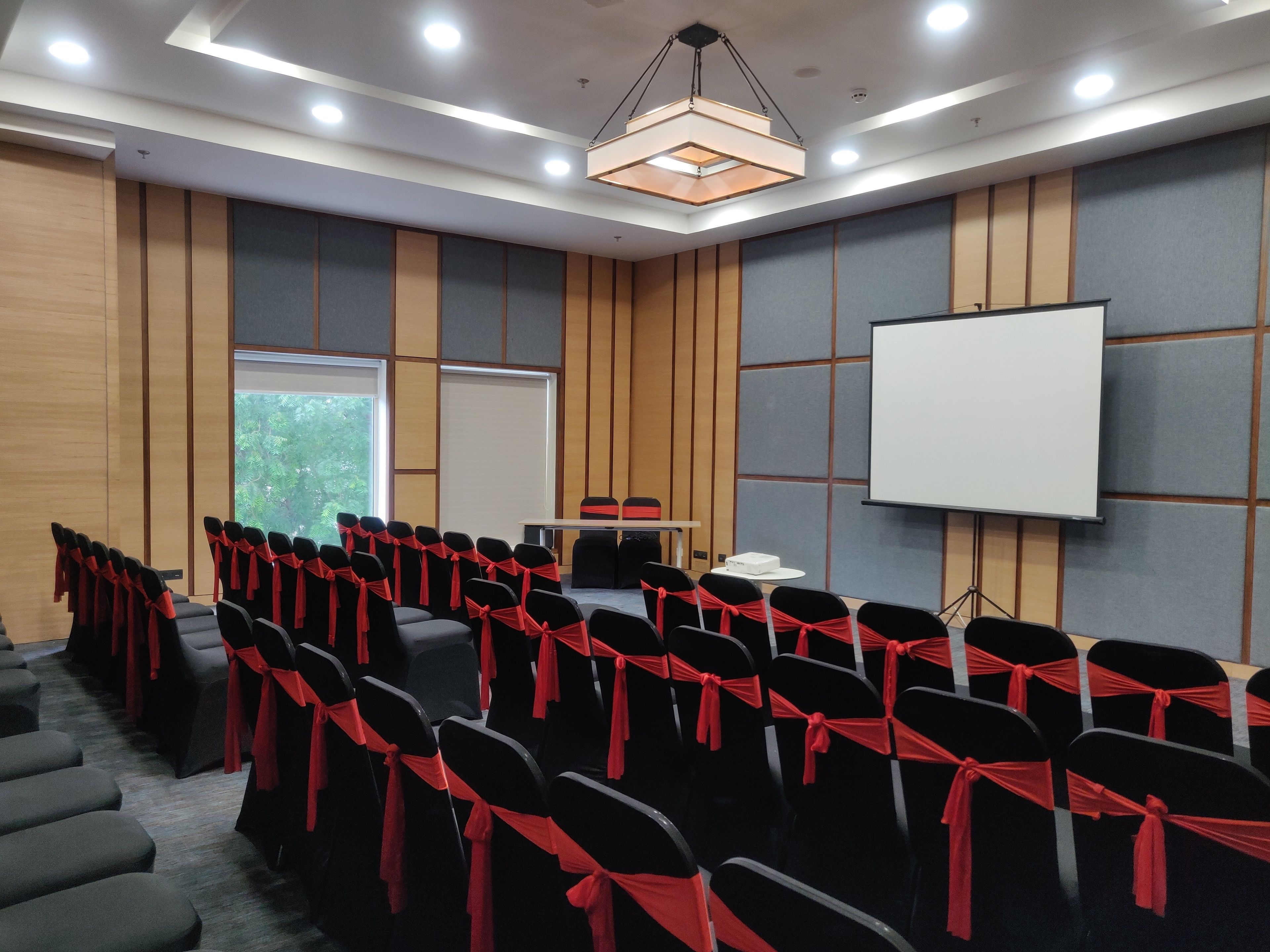 A conference room with rows of chairs, a projector screen, and a table with a cake.
