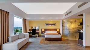 Una habitación de hotel moderna con una cama grande, un sofá, un escritorio y vistas a la ciudad.