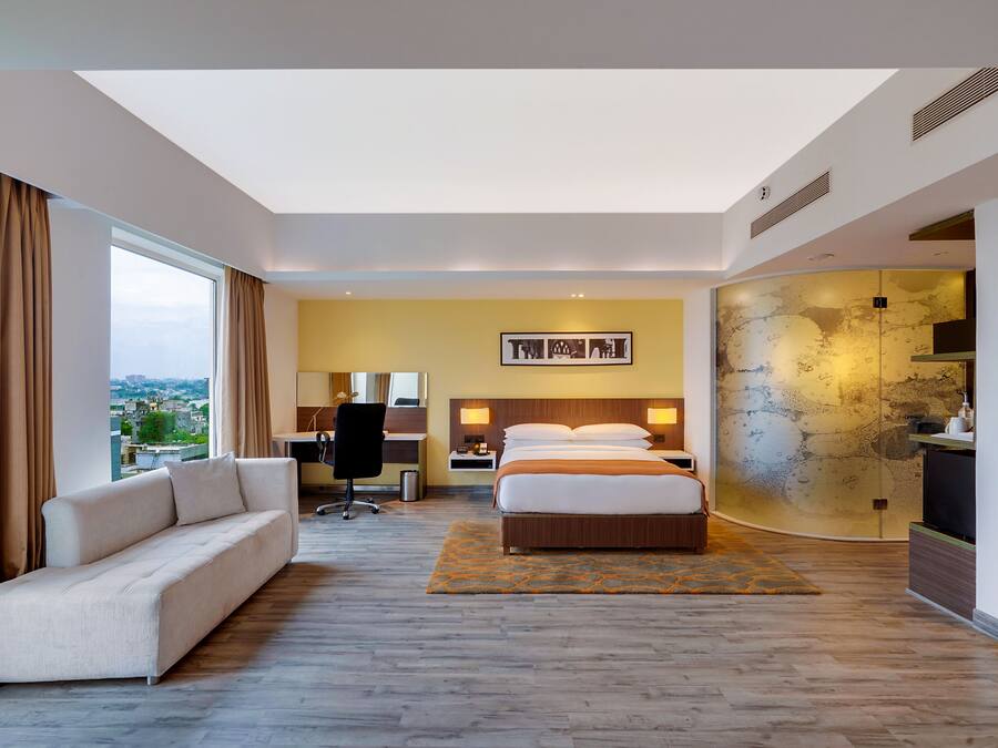 A modern hotel room with a large bed, a sofa, a desk, and a view of the city.