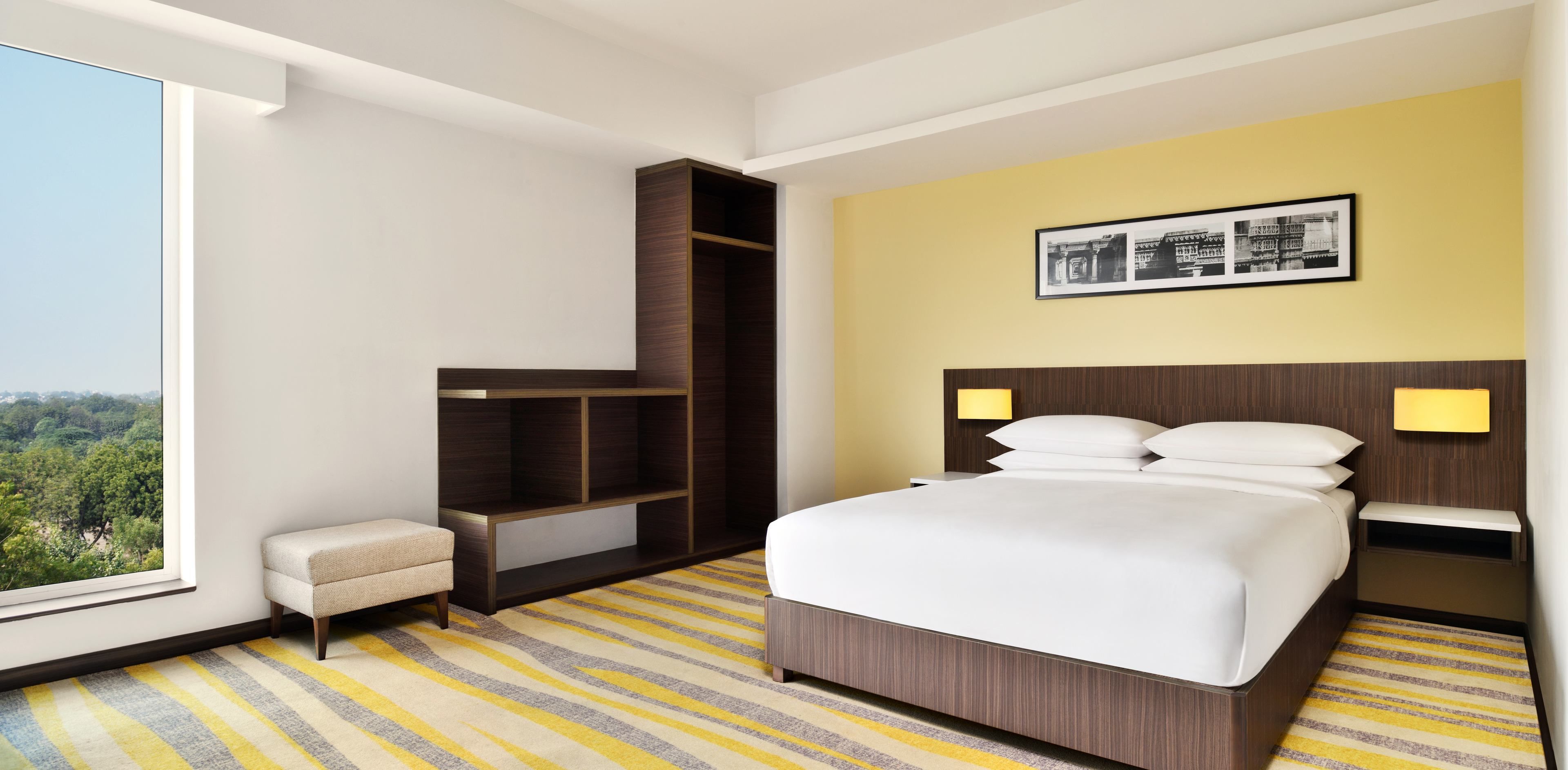 Habitación de hotel moderna con una cama grande, una banca, armario empotrado y vistas a la ciudad.