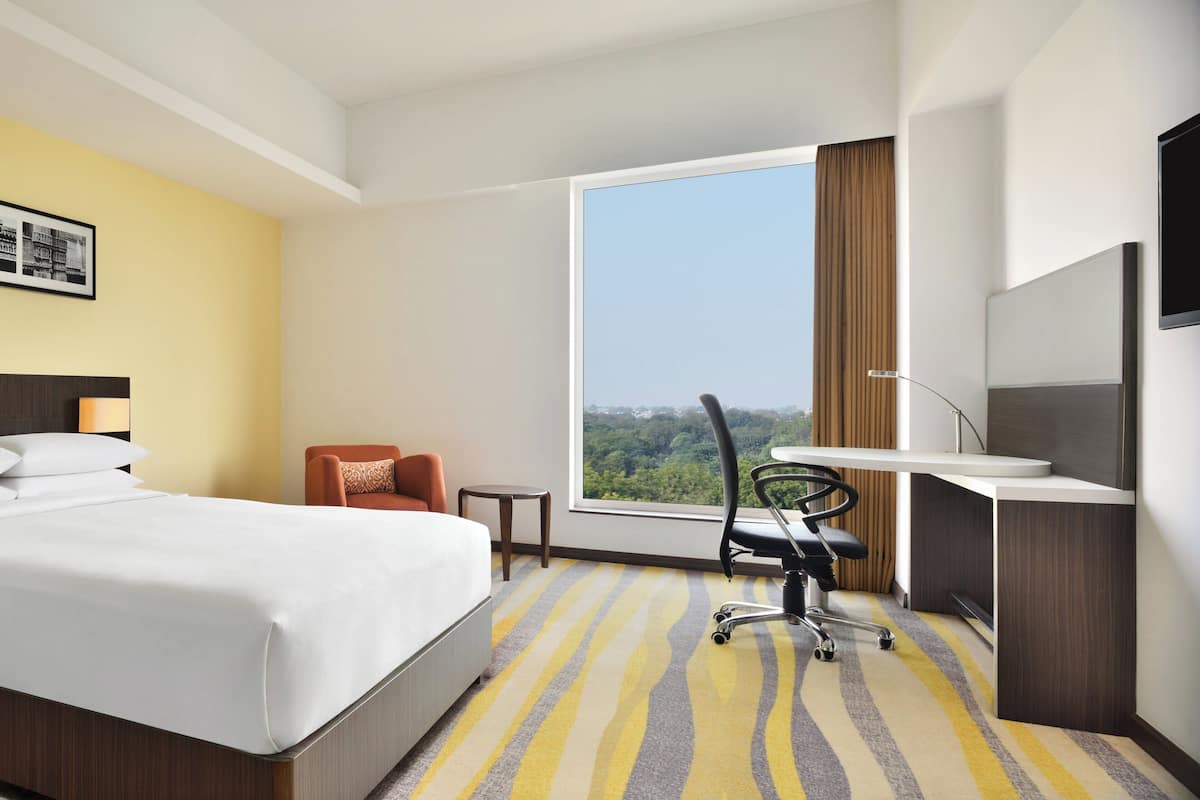 Ein Hotelzimmer mit einem Bett, einem Schreibtisch mit Stuhl, einem kleinen Tisch und einem großen Fenster mit Blick ins Freie.