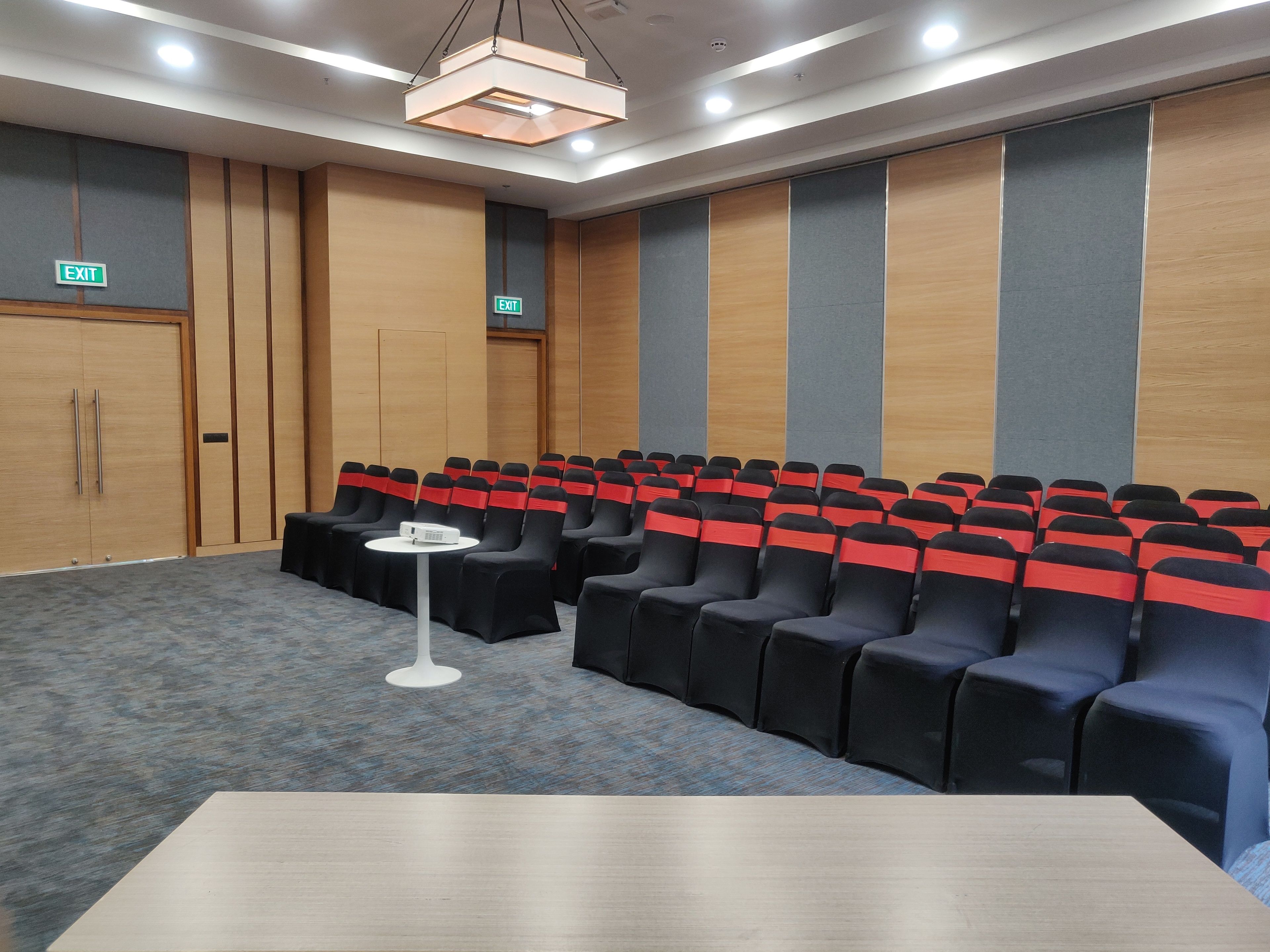 A conference room with rows of black chairs with red sashes, a white table, and an exit sign.