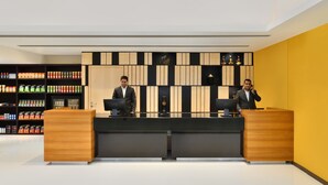 Una recepción con dos empleados, un interior moderno con un muro amarillo de acento y una estantería con aperitivos al fondo.