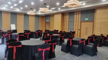 Un salón de conferencias con mesas redondas, sillas negras con cintas rojas y paneles de madera.