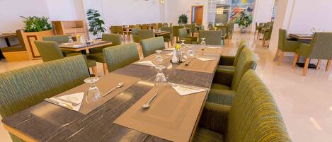 Un comedor moderno con mesas largas, sillas tapizadas en verde y un interior limpio y bien iluminado.