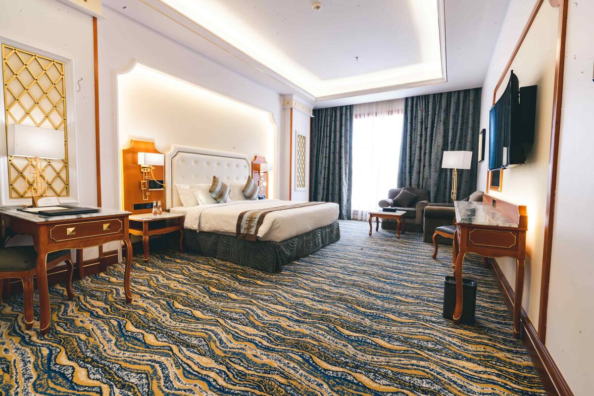 A hotel room with a large bed, a desk, a chair, a TV, and a window with curtains.