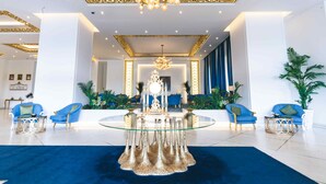 Un hall d’entrée spacieux, doté d’une table en verre au centre, de fauteuils bleus et d’un lustre décoratif.