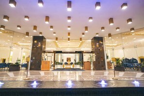 Een hotellobby met een receptiebalie, een zithoek en een fontein.