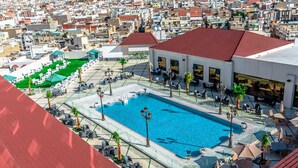 Un espace piscine aménagé sur le toit, avec des chaises longues et des parasols, entouré d’un paysage urbain.