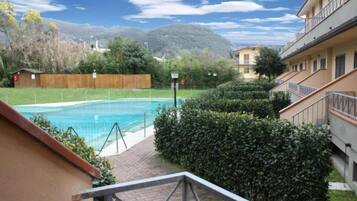Ein Schwimmbecken, umgeben von einem Holzzaun, mit Blick auf einen Berg und ein Gebäude mit Balkonen.