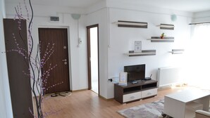 A modern living room with a wooden floor, a white sofa, a TV on a wooden stand, and a potted plant. - Alexys Residence 4 (Iasi)