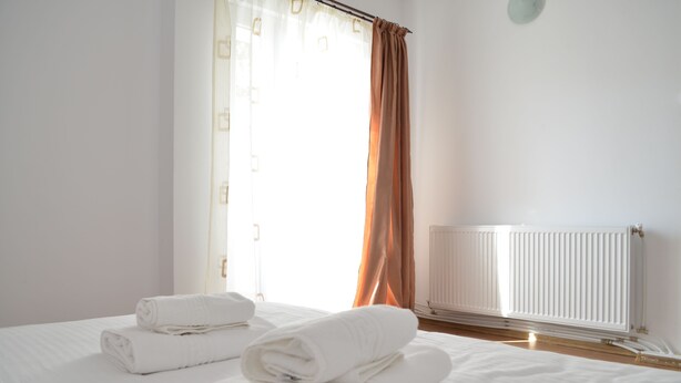 A hotel room with a bed, rolled white towels, a window with curtains, and a radiator. - Alexys Residence 4 (Iasi)