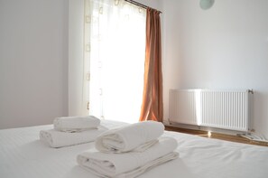 Une chambre d’hôtel avec un lit, des serviettes blanches pliées, une fenêtre avec des rideaux et un radiateur.