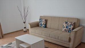 A beige sofa with floral cushions, a white side table, and a vase with branches. - Alexys Residence 4 (Iasi)