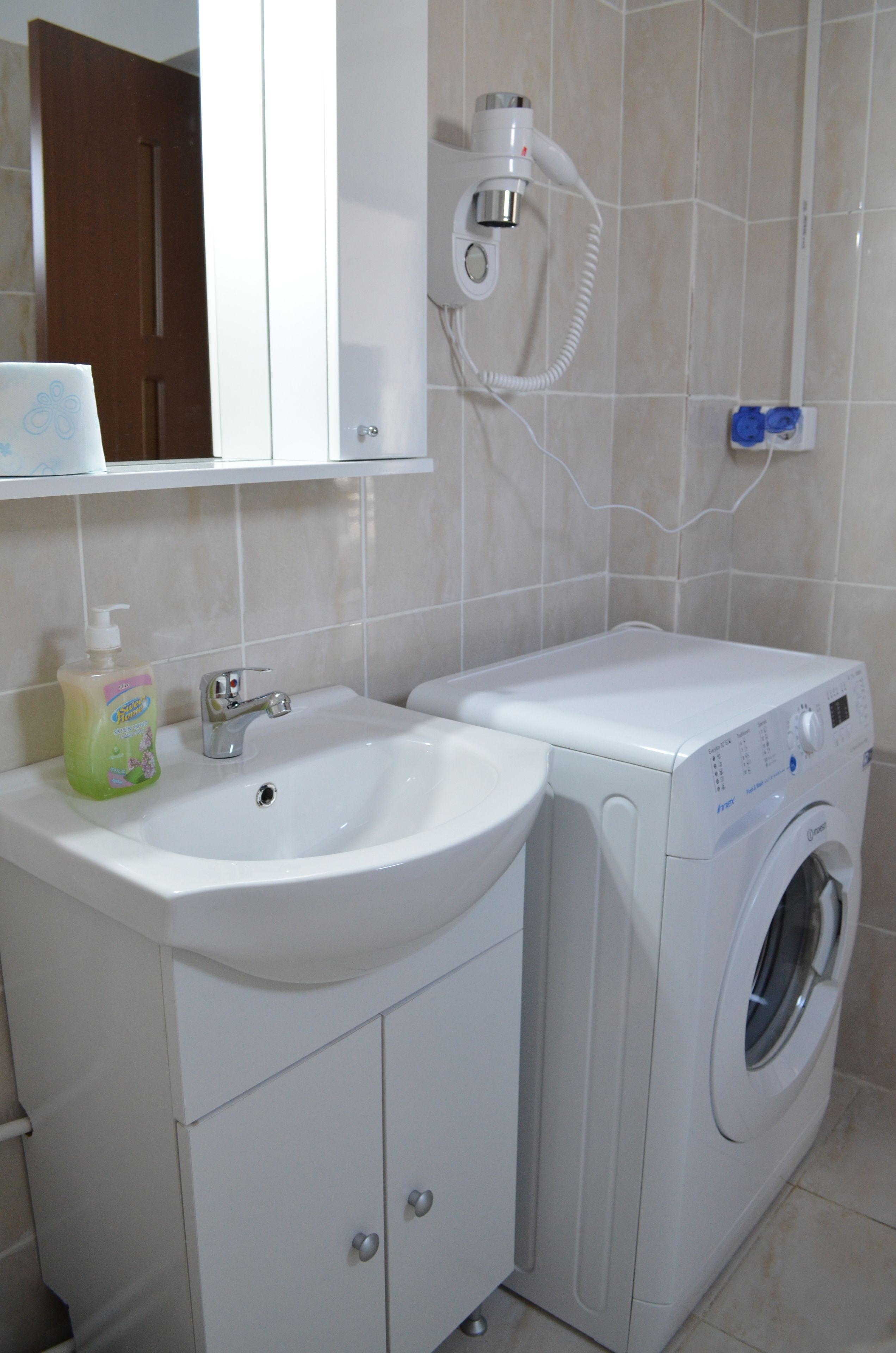 A bathroom with a sink, a washing machine, and a mirror.
