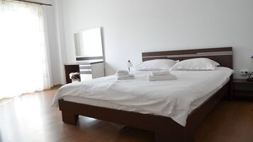 A neatly made bed with white linens and towels, a wooden headboard, a bedside table with a lamp, and a large mirror on the wall.