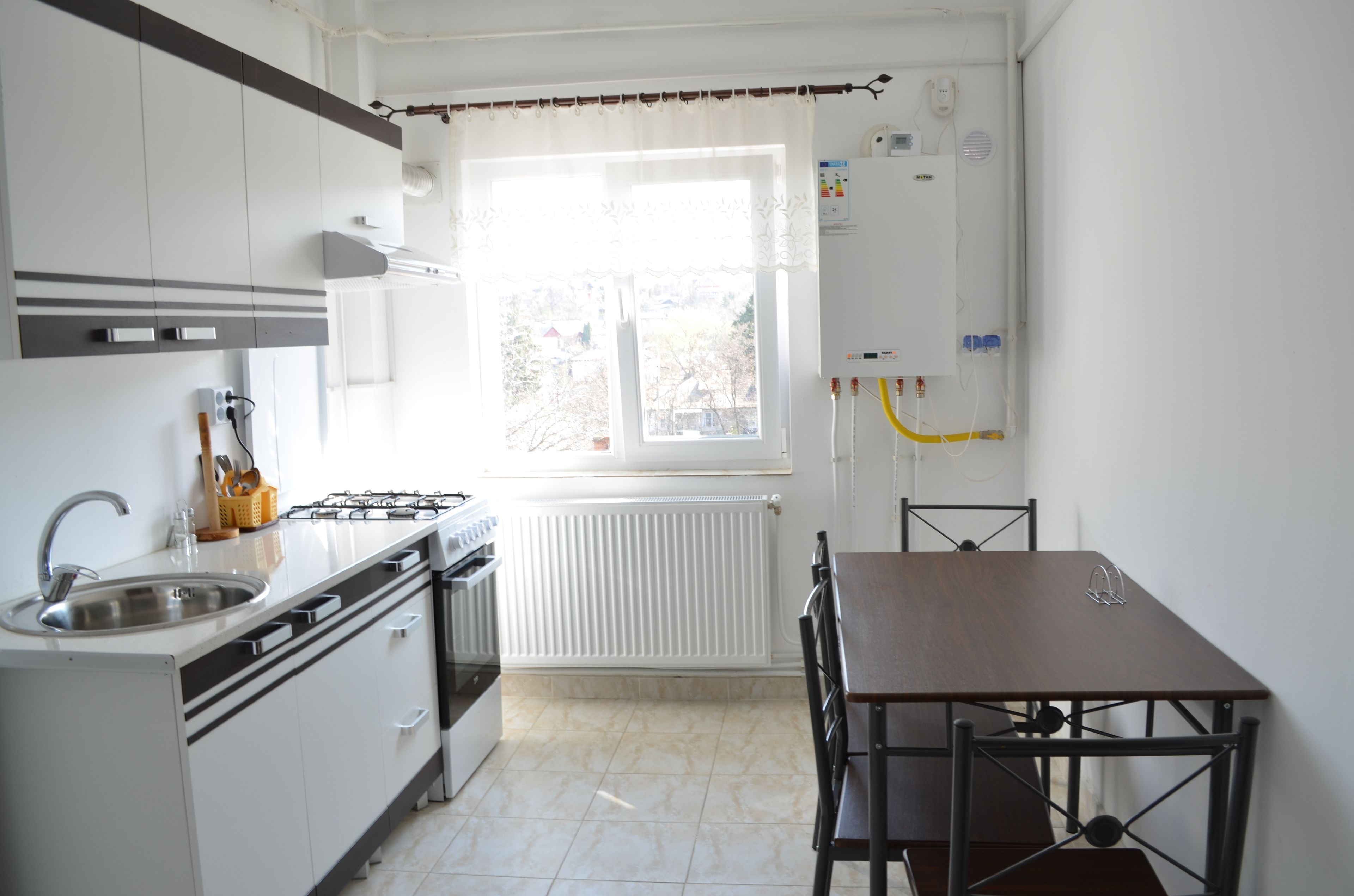 Una cocina con armarios blancos, una estufa, un lavamanos y una ventana con cortinas.
